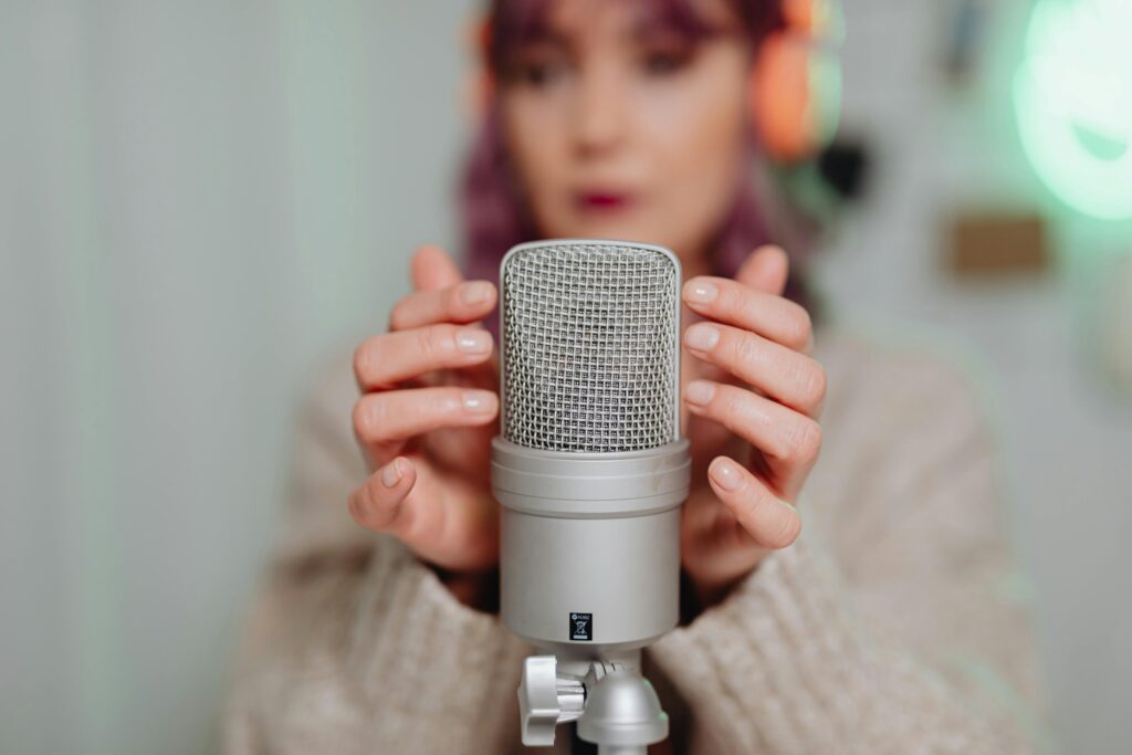 A woman in headphones uses a studio microphone for ASMR recording indoors.